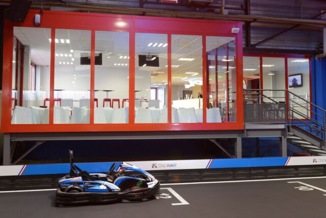 Karturi colorate în viteză pe o pistă de karting acoperită, delimitată de anvelope de protecție