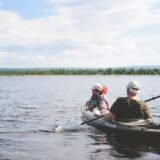 Colegi de muncă vâslind împreună în caiace pe un lac liniștit, în timpul unei zile de teambuilding