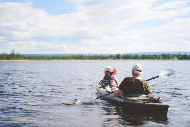 Colegi de muncă vâslind împreună în caiace pe un lac liniștit, în timpul unei zile de teambuilding