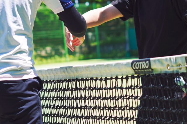 Doi jucători de tenis la dublu poziționați la fileu, pregătiți să intercepteze mingea adversarilor