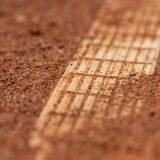 Teren de tenis din zgură roșie, cu liniile albe proaspăt periate și fileul în fundal